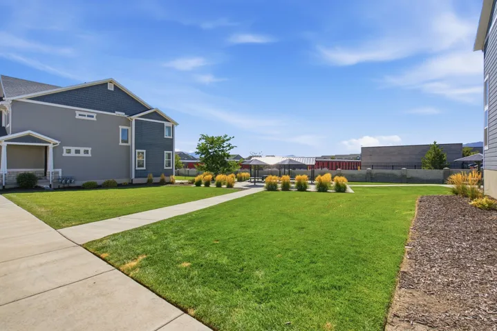 Expansive green space featuring a concrete pathway, landscaped shrubs, and a covered patio area