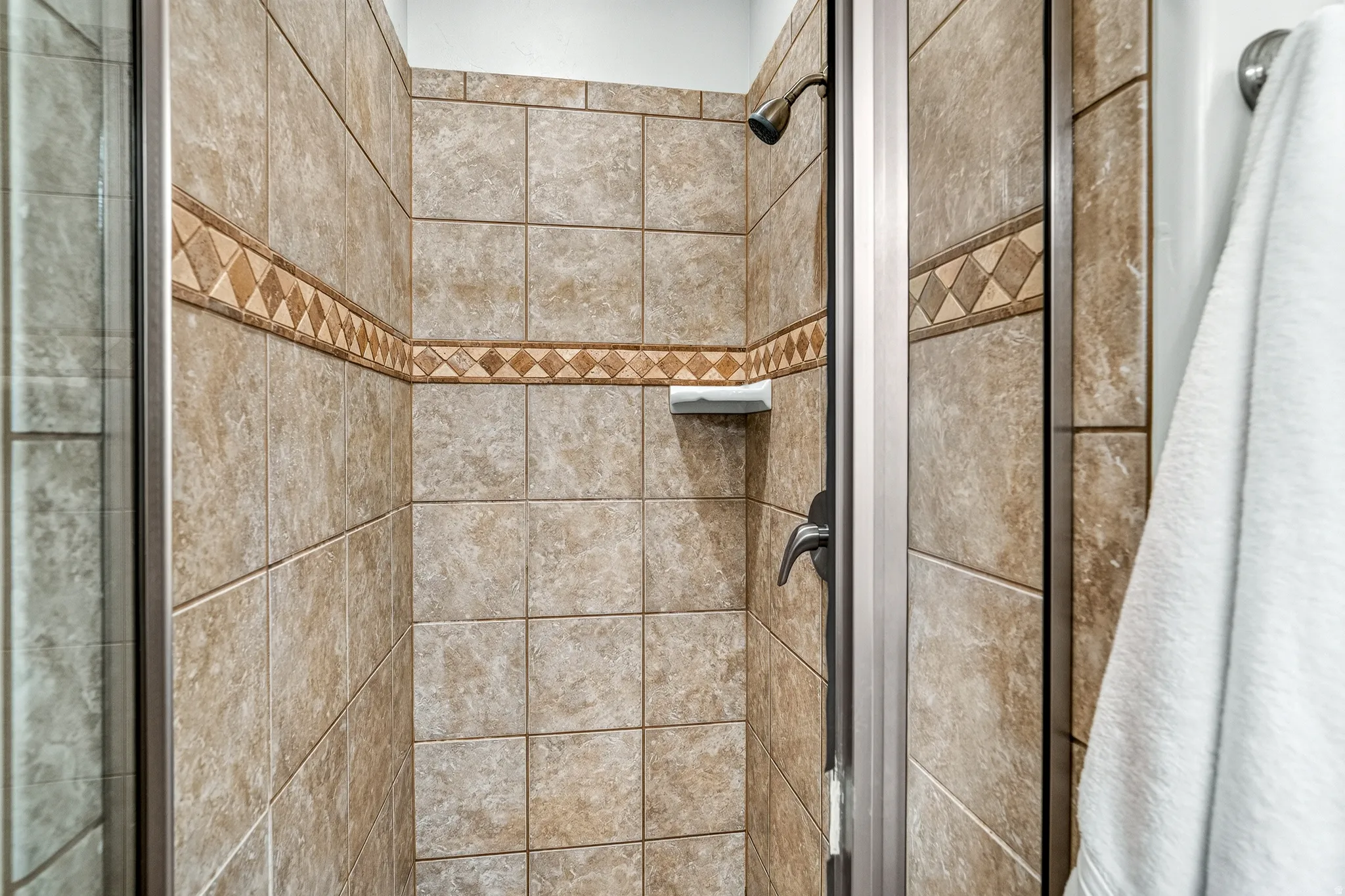 Tiled shower enclosure featuring a decorative accent band, integrated soap dish, and a bronze-finish shower head with coordinating controls