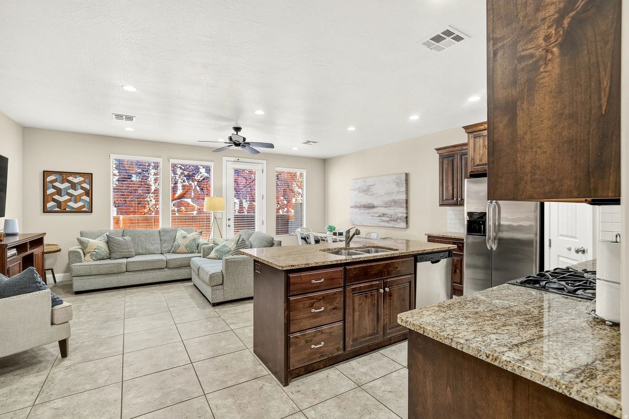 Open-concept living space featuring a kitchen with granite countertops, wood cabinetry, and stainless steel appliances