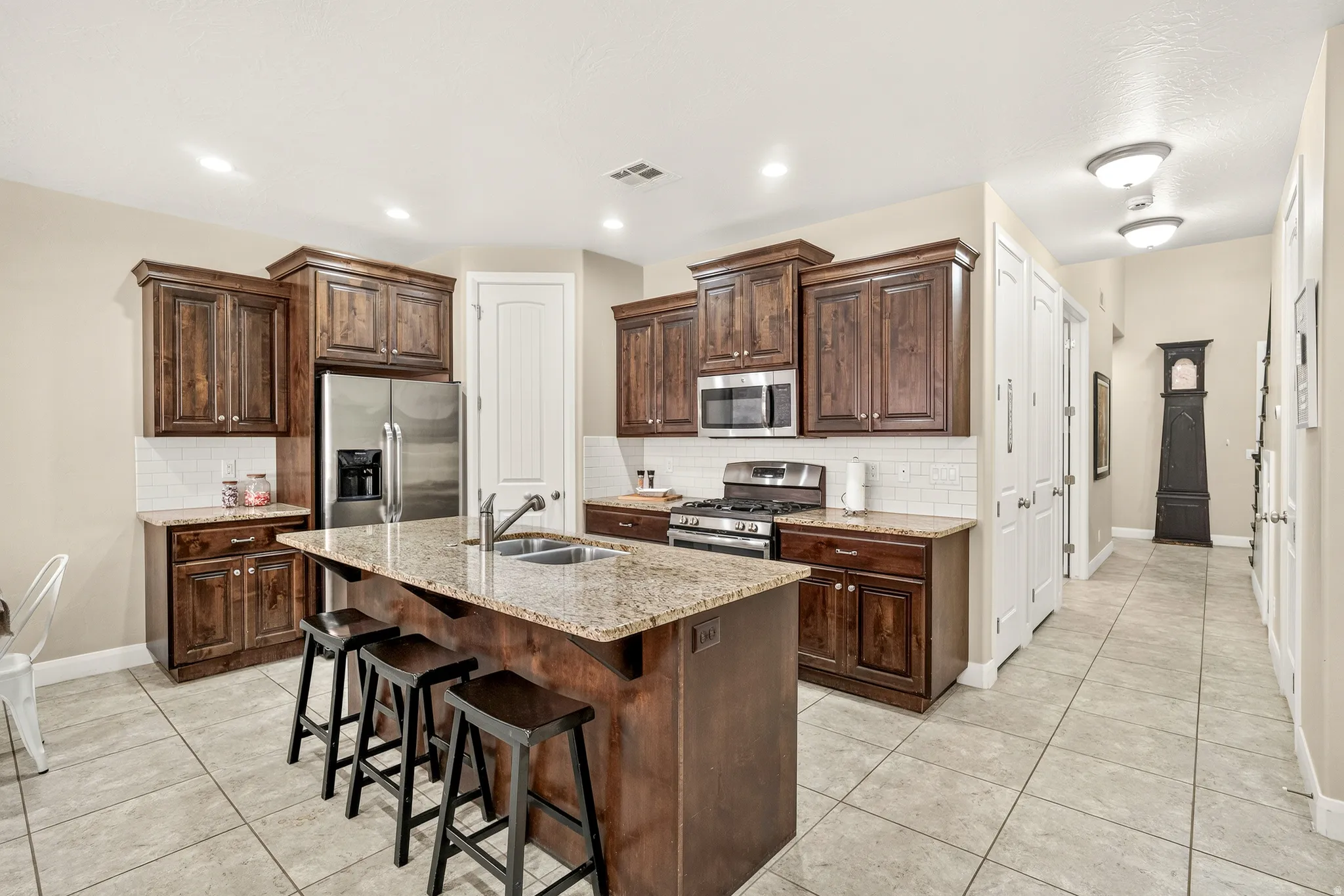 Kitchen featuring rich wood cabinetry, stainless steel appliances, a center island with sink, and light-toned tile flooring