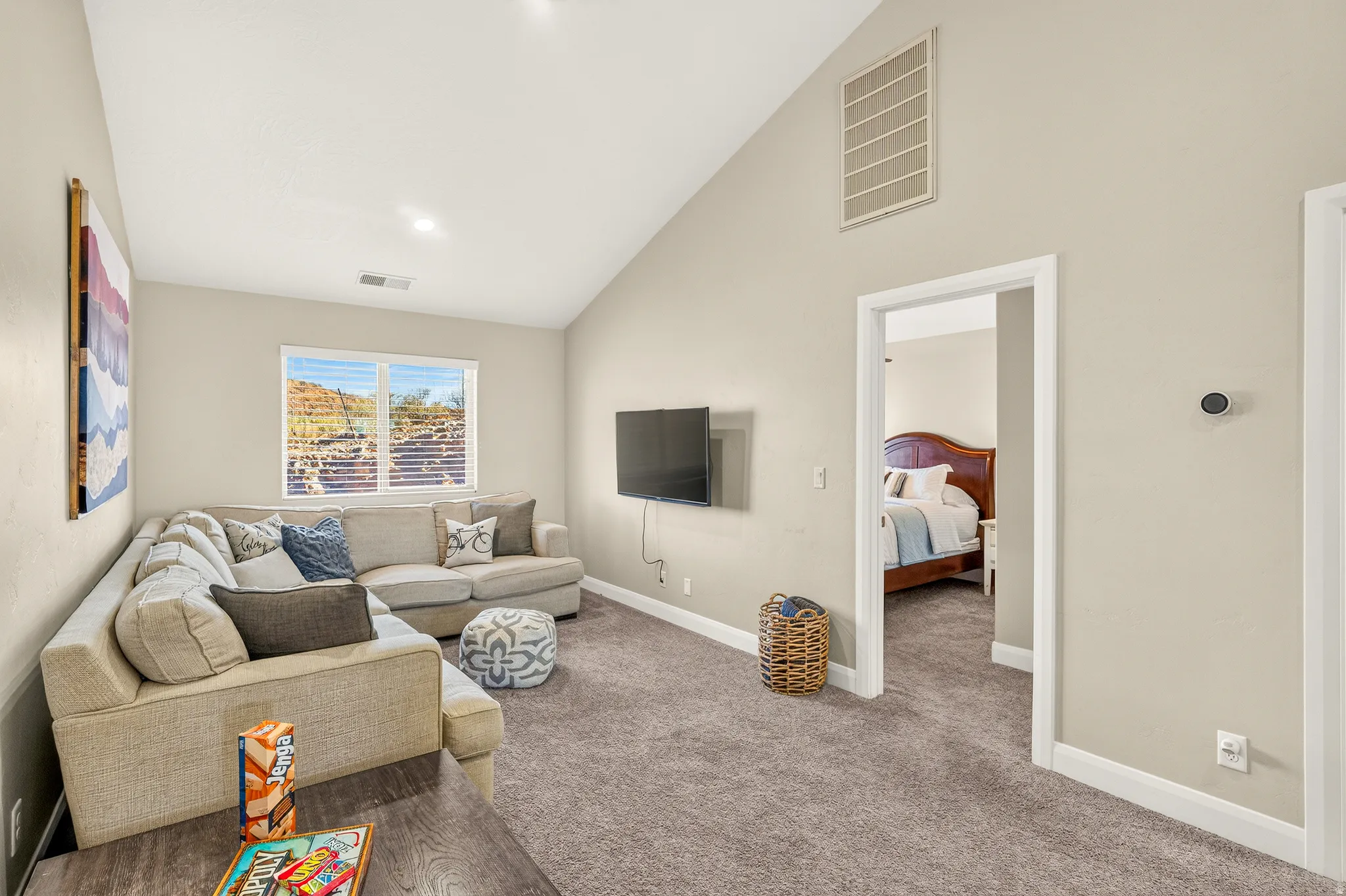 Vaulted ceiling, recessed lighting, wood-finish flooring, wall-mounted television, and a window with horizontal blinds