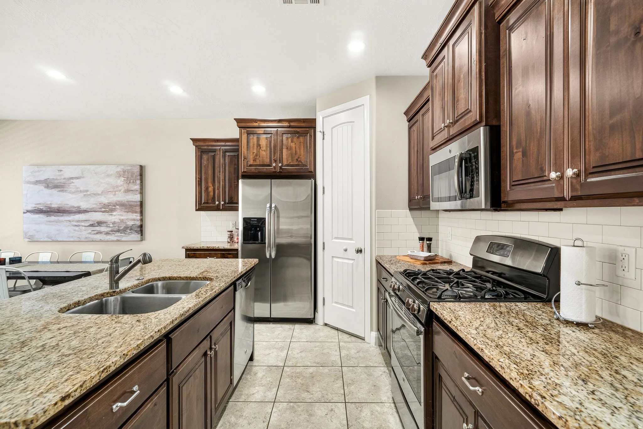 Kitchen with granite countertops, stainless steel appliances, dark wood cabinetry, white subway tile backsplash, and tile flooring