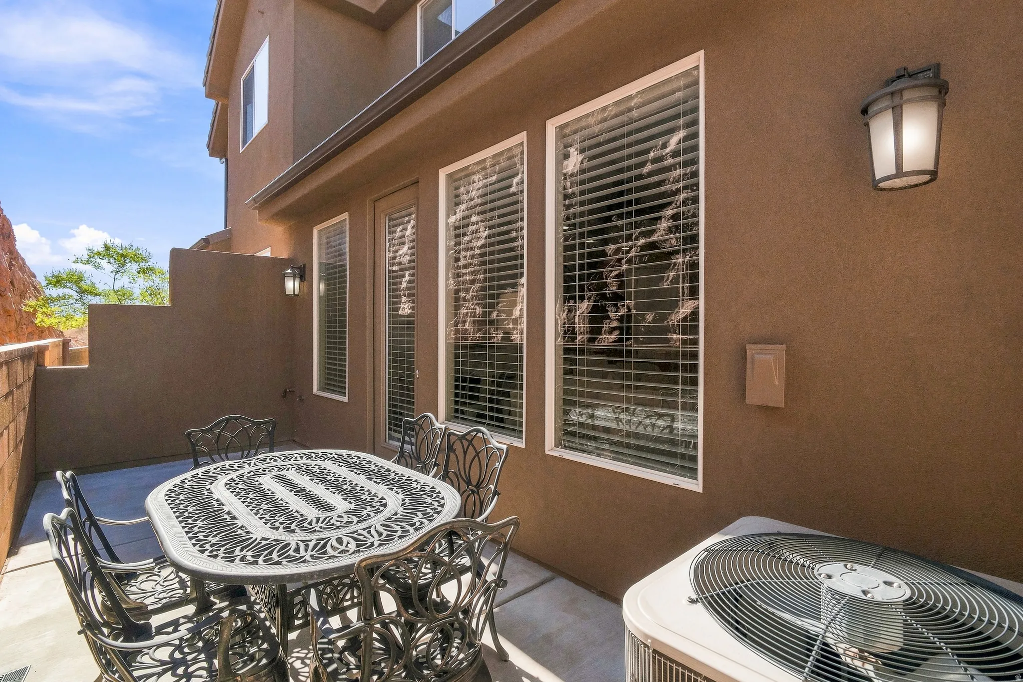 Concrete patio with stucco exterior, multiple large windows, and an exterior wall light fixture