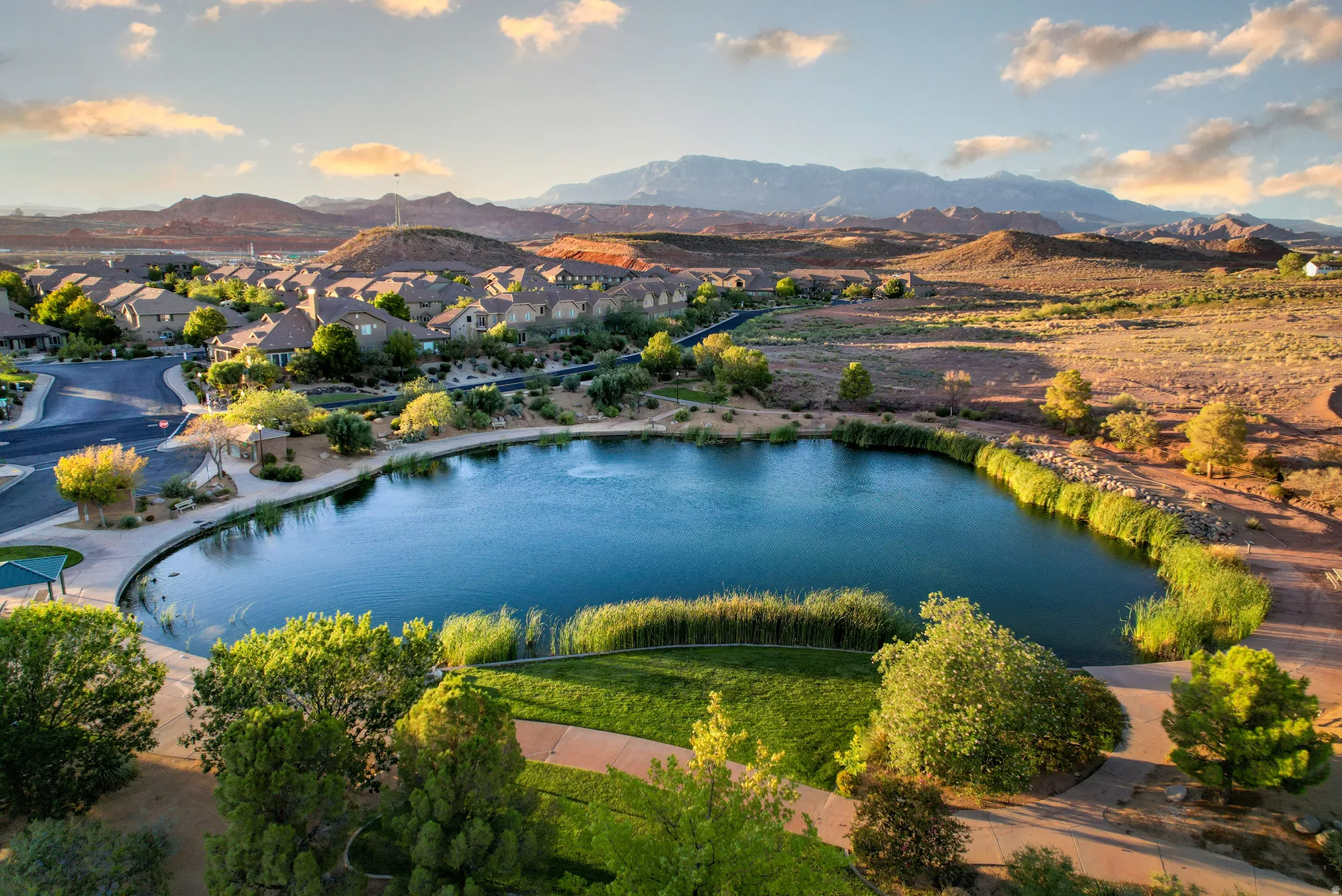 Expansive community lake with surrounding green spaces, paved pathways, and mature landscaping, set against a backdrop of distant mountains
