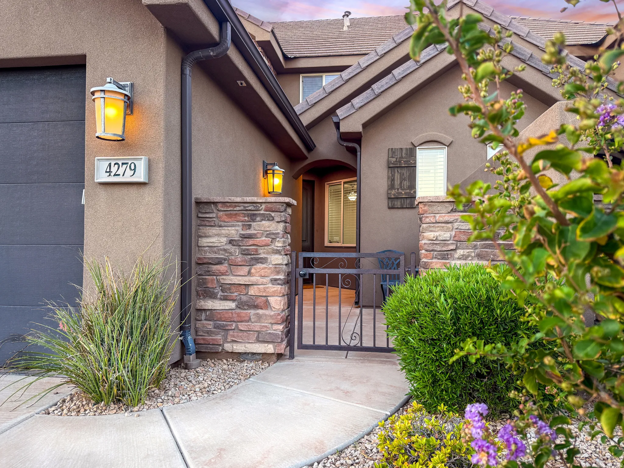 Stucco exterior with stone veneer accents, concrete pathway, and wrought iron gate