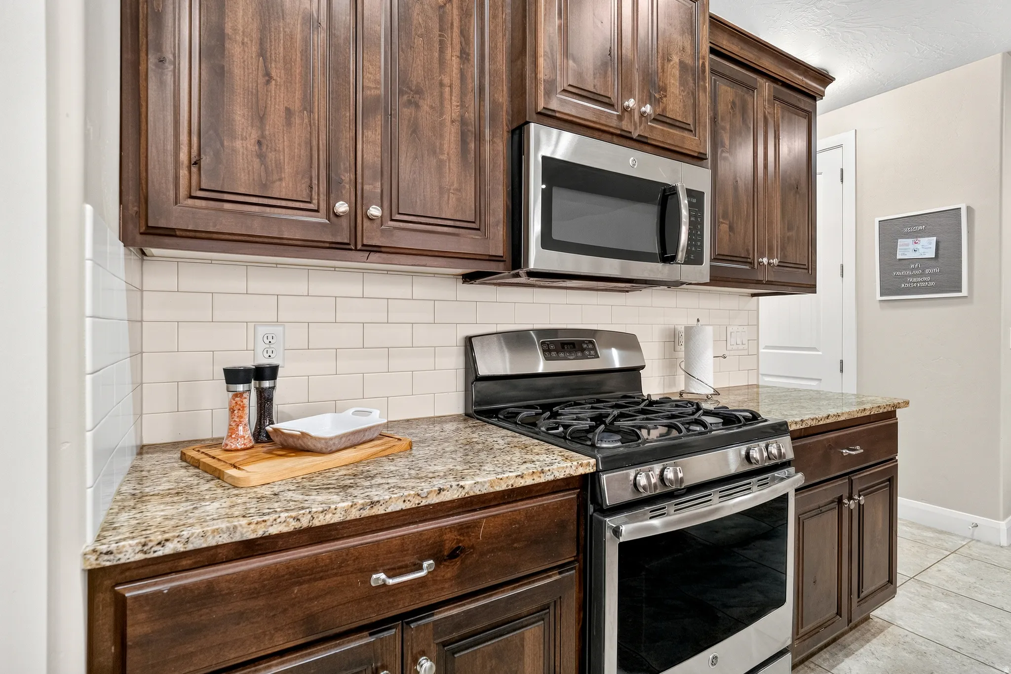 Dark wood-finish cabinetry, stainless steel microwave, stainless steel range, light-toned countertops, and subway tile backsplash