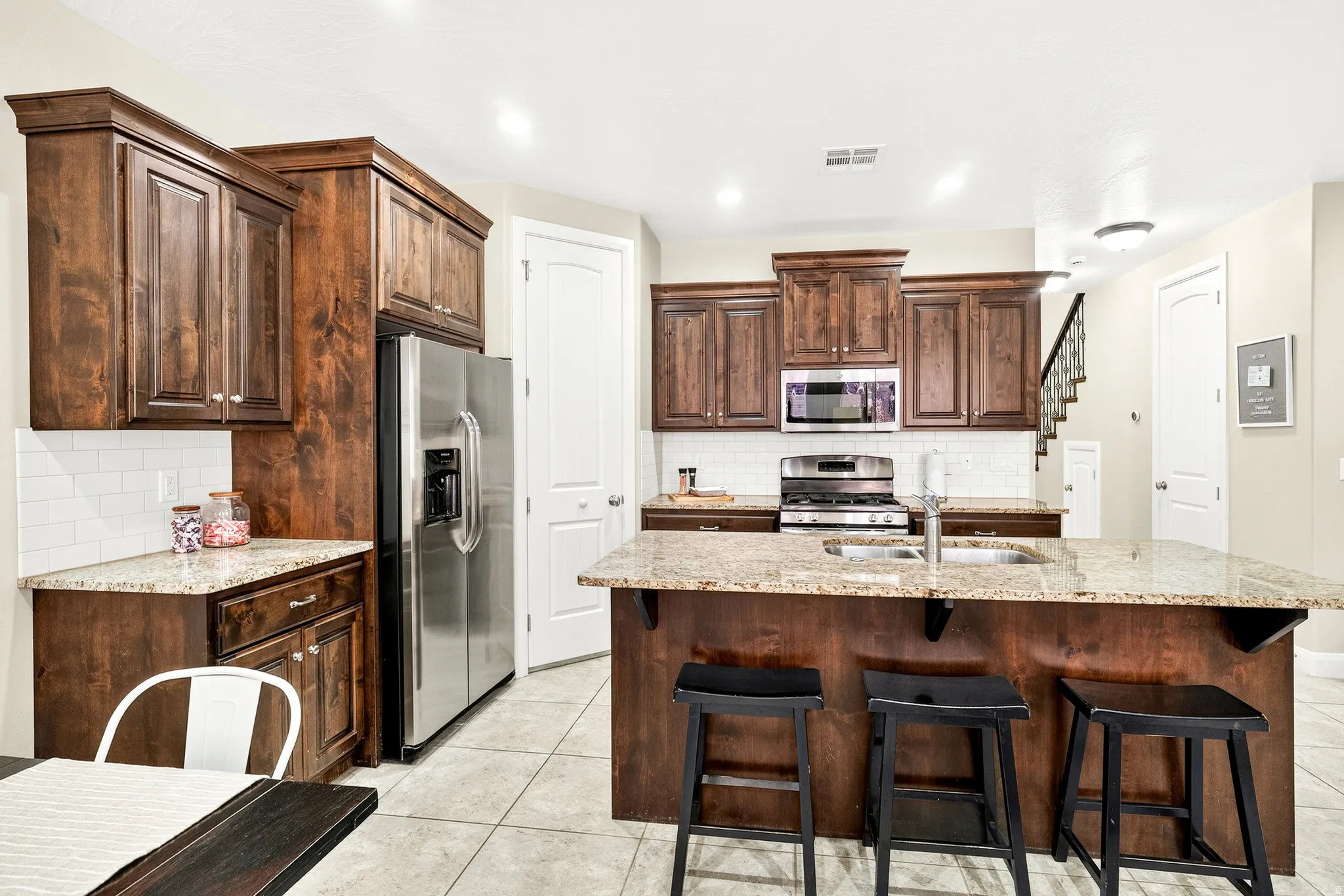 Kitchen featuring wood cabinetry, stainless steel appliances, a center island with bar seating, light-colored tile flooring, and a white subway tile backsplash
