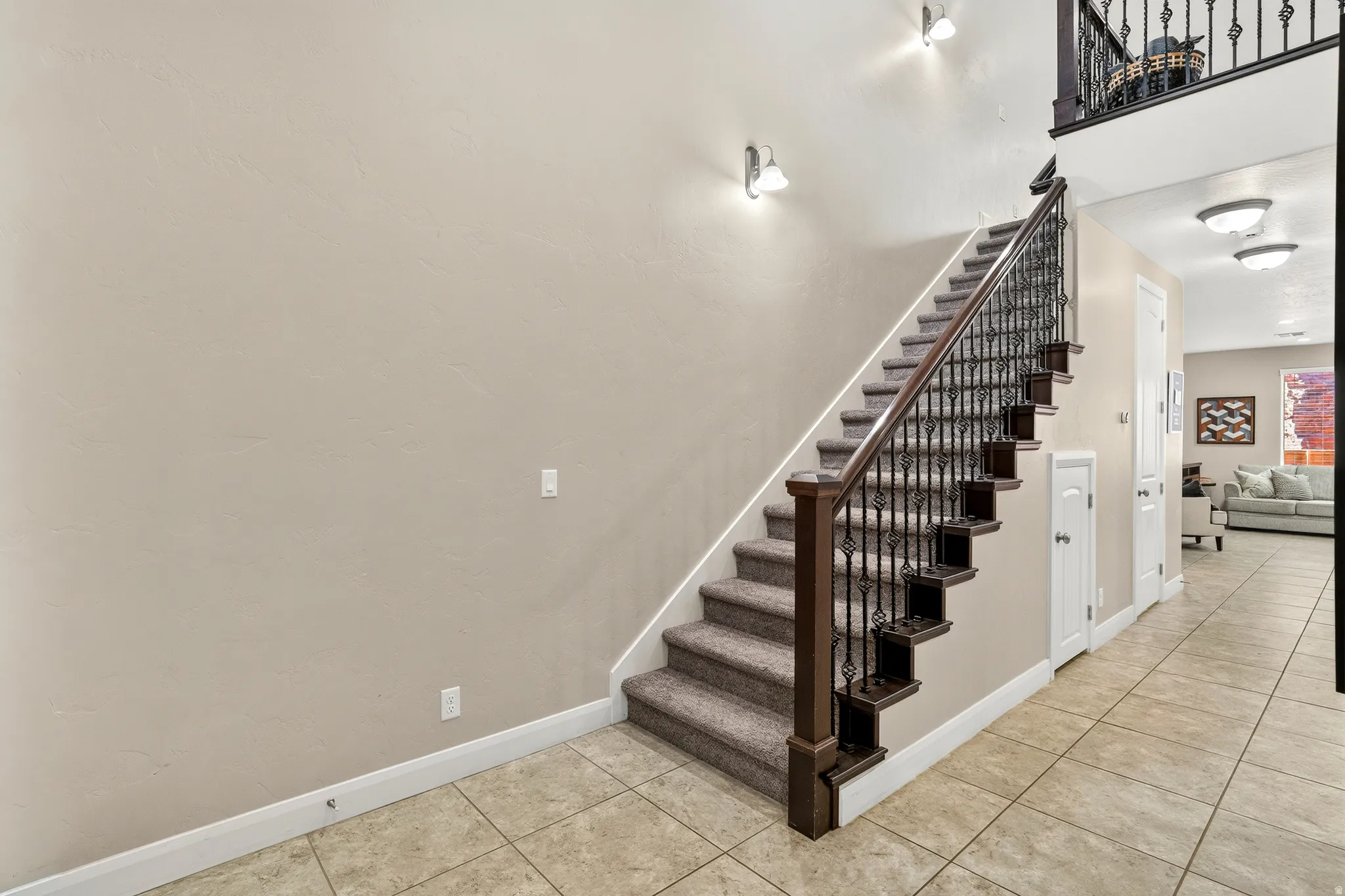 Staircase with wrought iron balusters and carpeted treads, complemented by ceramic tile flooring