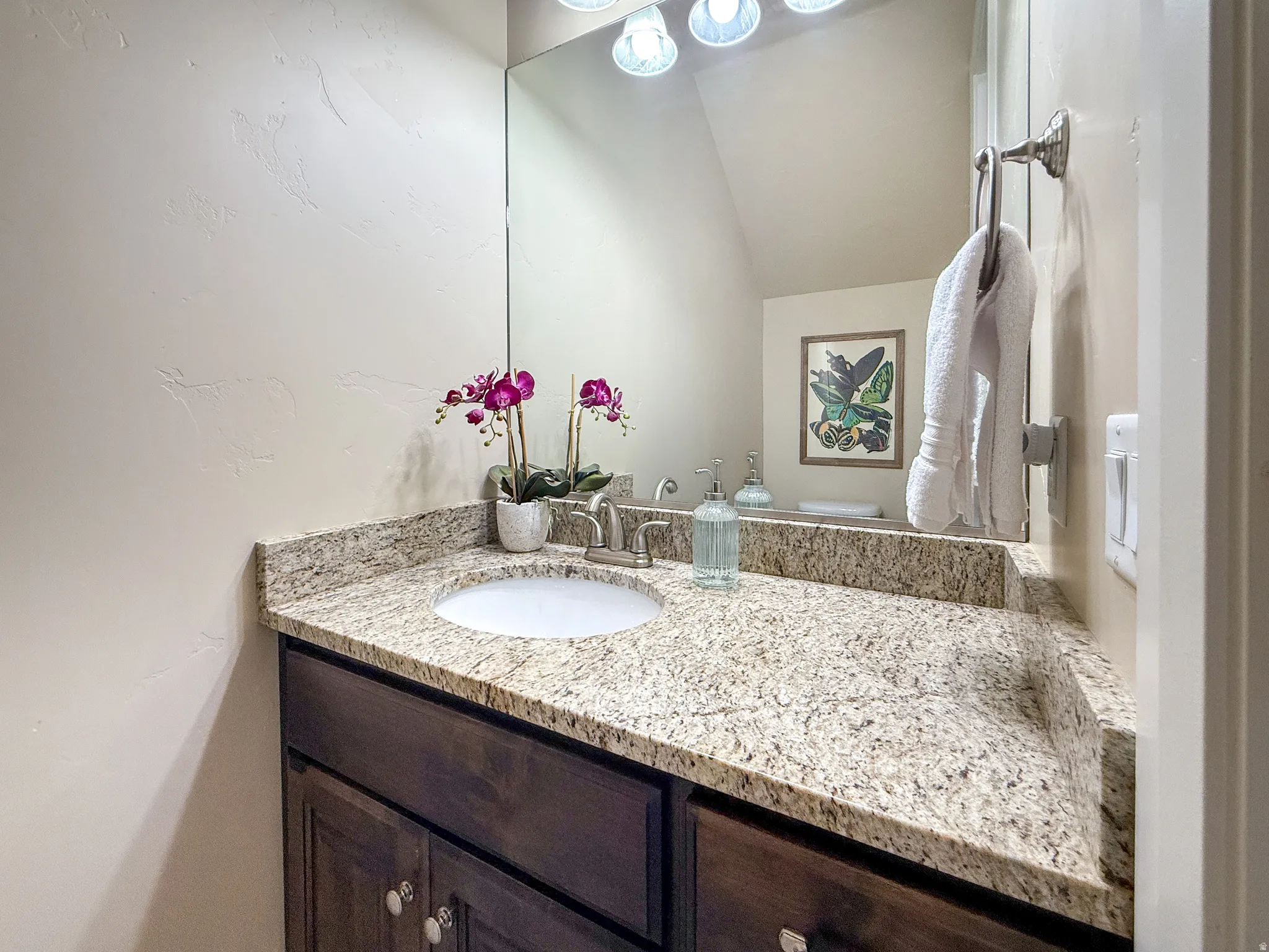 Granite-look countertop with integrated sink, dark wood-finish vanity, and a large wall-mounted mirror with overhead lighting