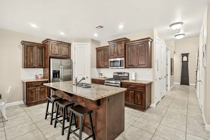 Kitchen featuring rich wood cabinetry, stainless steel appliances, a center island with sink, and light-toned tile flooring