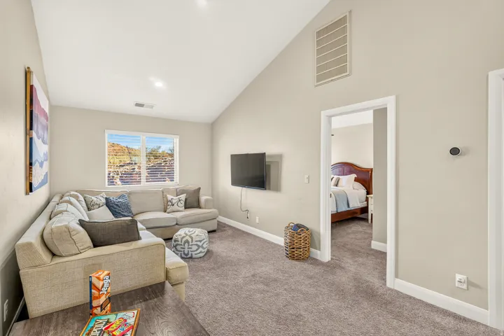 Vaulted ceiling, recessed lighting, wood-finish flooring, wall-mounted television, and a window with horizontal blinds