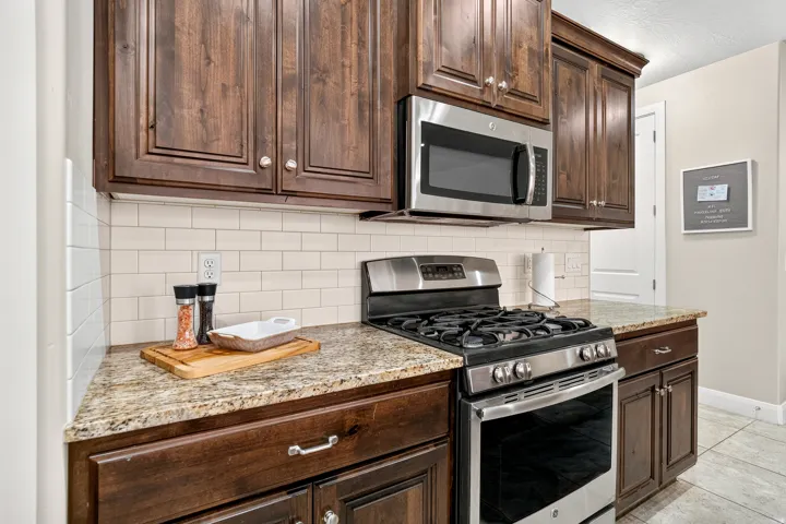 Dark wood-finish cabinetry, stainless steel microwave, stainless steel range, light-toned countertops, and subway tile backsplash