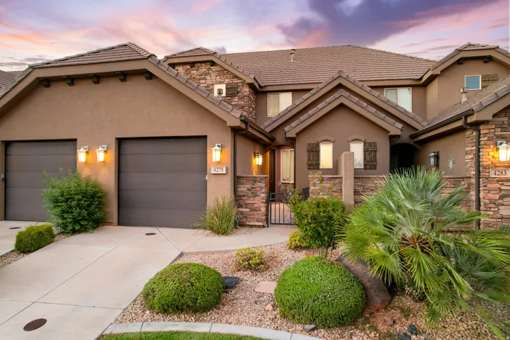 Stucco exterior with stone accents, a tiled roof, multiple garage doors, and decorative outdoor lighting