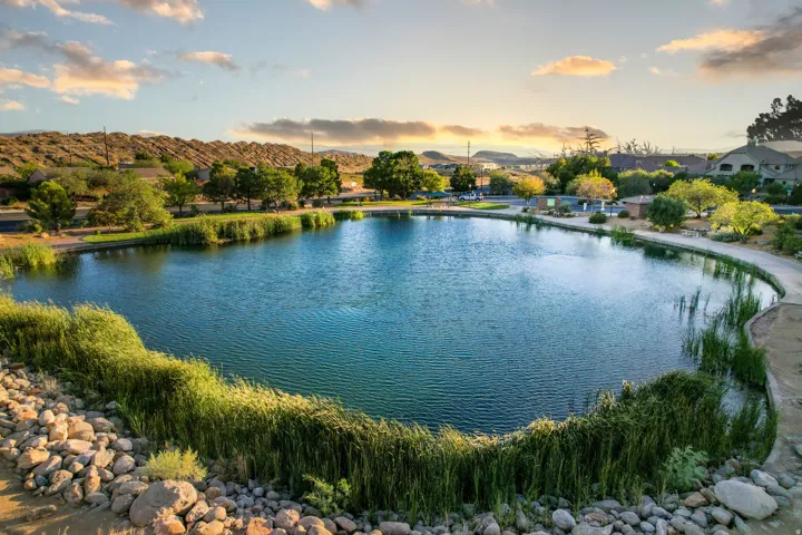 Community lake with walking path, surrounded by mature trees and natural landscaping