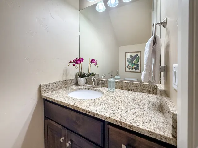 Granite-look countertop with integrated sink, dark wood-finish vanity, and a large wall-mounted mirror with overhead lighting