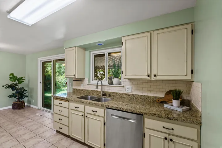 Kitchen featuring a double basin sink, granite-style countertops, white subway tile backsplash, and cream cabinetry with dark hardware