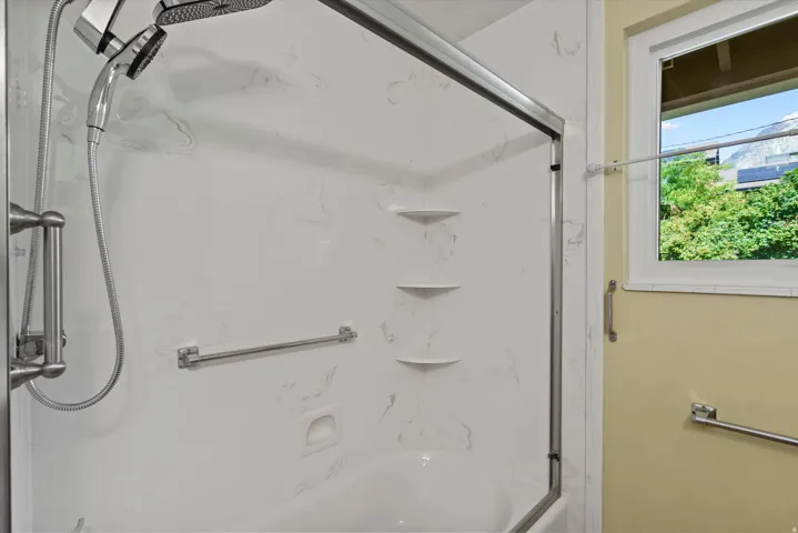 Bathtub and shower combination with a sliding glass enclosure, integrated shelving, and a wall-mounted showerhead with an additional handheld sprayer