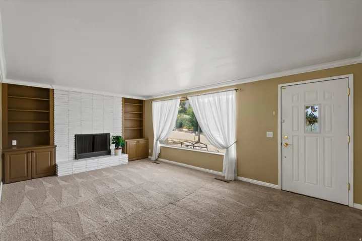 Carpeted living space featuring a brick-surround fireplace, built-in shelving, and a large window