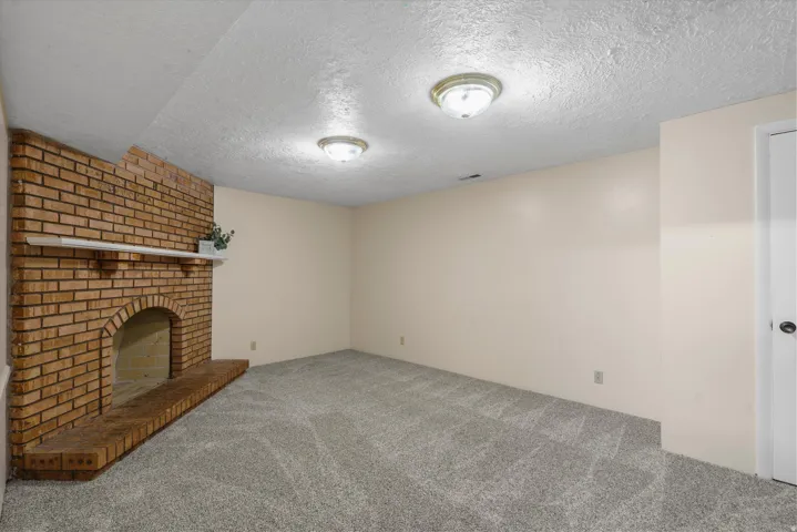 Brick fireplace with a white mantel, neutral wall paint, and gray carpeting