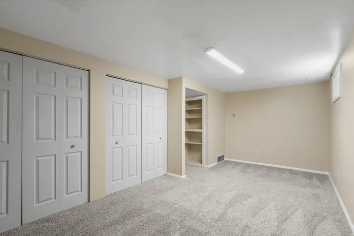 Neutral-toned walls, carpeted flooring, built-in shelving, two sets of bi-fold closet doors, and recessed window
