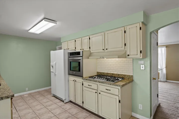 Kitchen featuring built-in stainless steel oven, gas range, tile backsplash, granite-finish countertops, and cream cabinetry