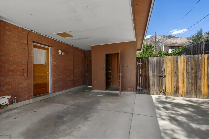 Covered carport with a concrete slab, brick exterior wall, and a wood-paneled door