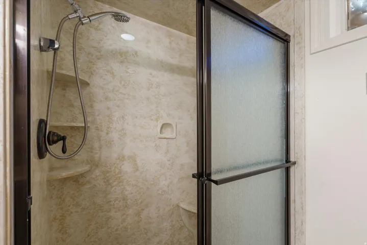 Enclosed shower featuring a handheld showerhead, integrated shelving, and a textured wall surround