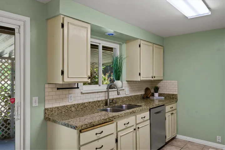 Kitchen featuring granite-style countertops, subway tile backsplash, a stainless steel double basin sink, and white cabinetry