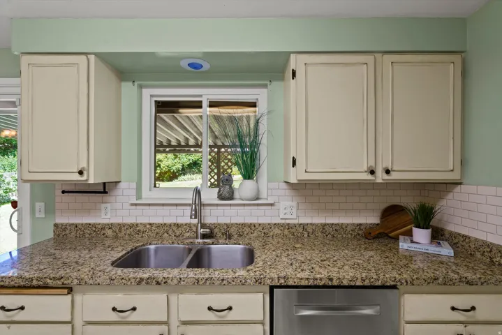 Kitchen featuring granite countertops, a stainless steel double-basin sink, white subway tile backsplash, cream cabinetry, and a stainless steel dishwasher