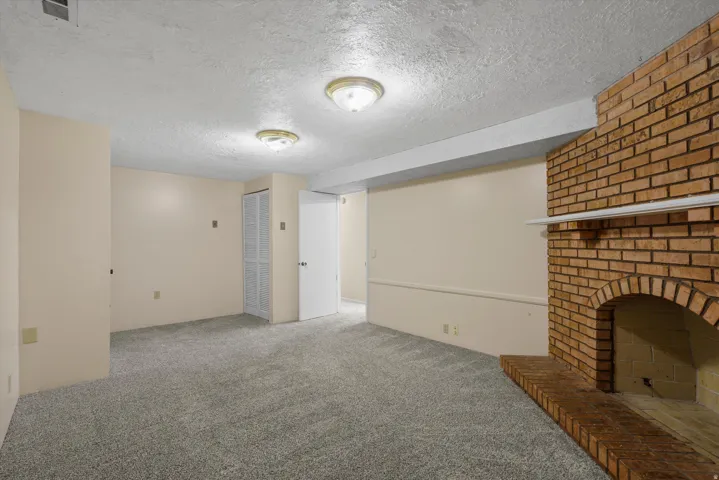 Brick-clad fireplace with hearth, textured ceiling with flush-mount lighting, and light gray carpeting