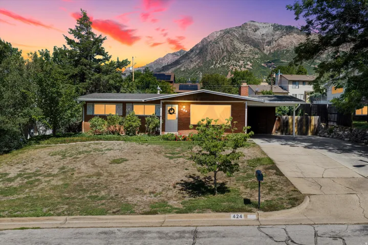 Brick exterior with a covered carport, mature trees, and a mountain backdrop
