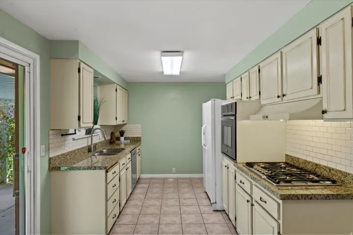 Galley kitchen featuring cream cabinetry, granite countertops, subway tile backsplash, and tile flooring