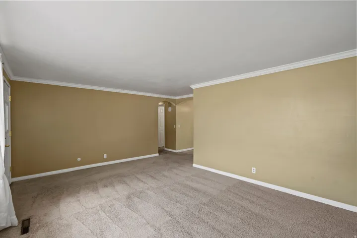 Spacious room with neutral-toned walls, crown molding, and carpeted flooring