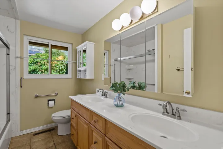 Dual vanity with white undermount sinks, wood-finish cabinetry, and a full-width mirror