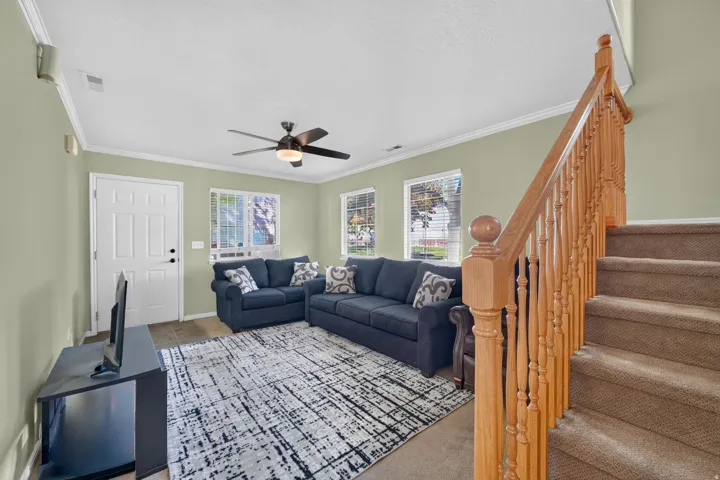 Inviting living area featuring a ceiling fan with light, multiple windows, and a staircase with wood newel posts and balusters