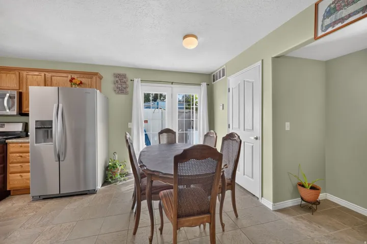 Kitchen and dining area featuring tile flooring, wood cabinetry, stainless steel refrigerator, and double French doors with exterior access