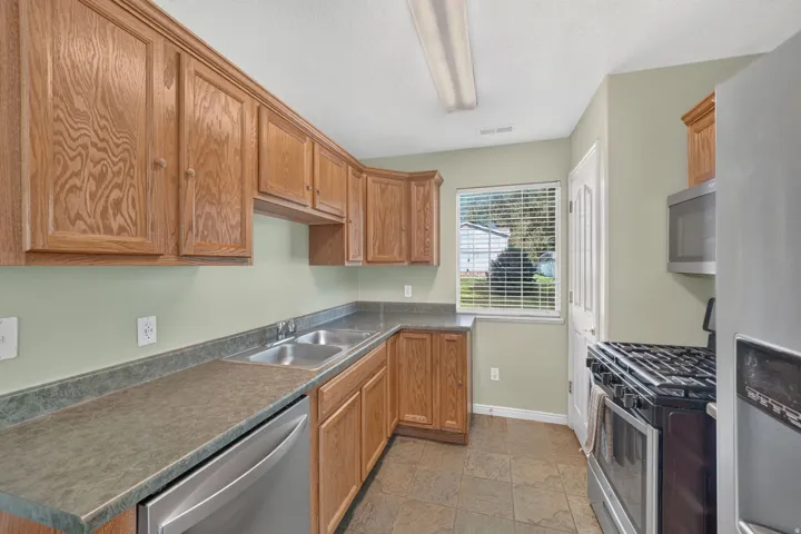 Wood-finish cabinetry, stainless steel double basin sink, stainless steel dishwasher, tile flooring, and a built-in microwave