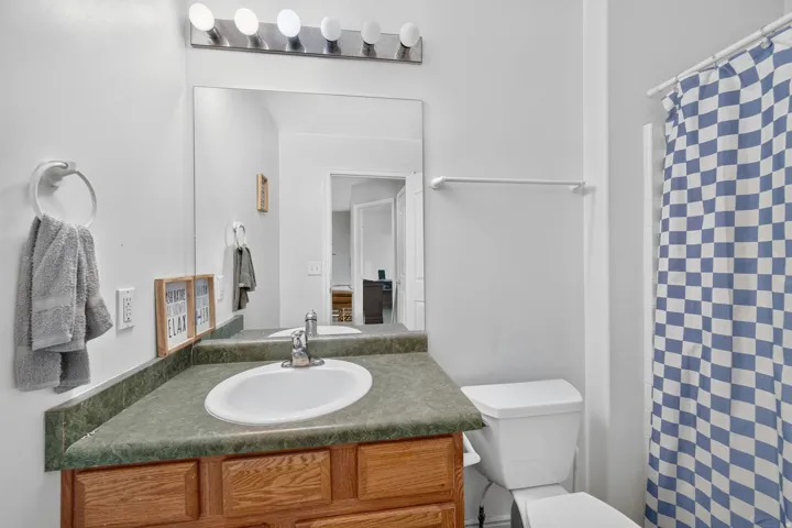 White wall paint, wood-finish vanity with drawer storage, built-in oval sink, green countertop, and a vanity mirror with overhead lighting
