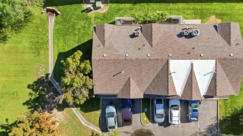 Gable roofline with asphalt shingles, paved parking area, and manicured green spaces