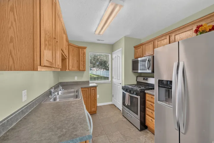 Kitchen featuring wood-finish cabinetry, stainless steel appliances, dual basin sink, and tiled flooring