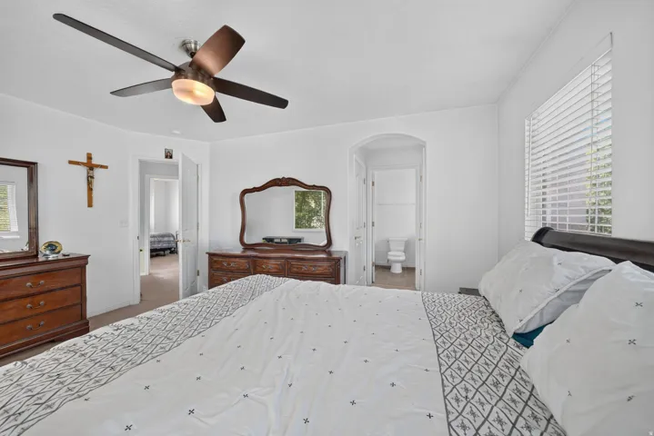 Ceiling fan with integrated lighting, arched doorway, window with horizontal blinds, and a private attached bathroom