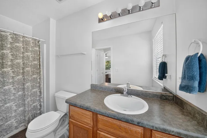 Bathroom featuring a wood-finish vanity with an integrated sink, a large mirror, and a window with blinds