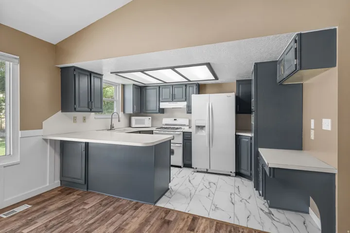 Kitchen featuring dark cabinetry, white countertops, built-in appliances, a central island, and mixed flooring