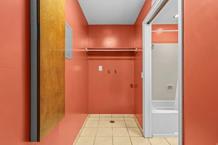 Utility area featuring tiled flooring, a clothing rod, wall-mounted hooks, and an electrical panel