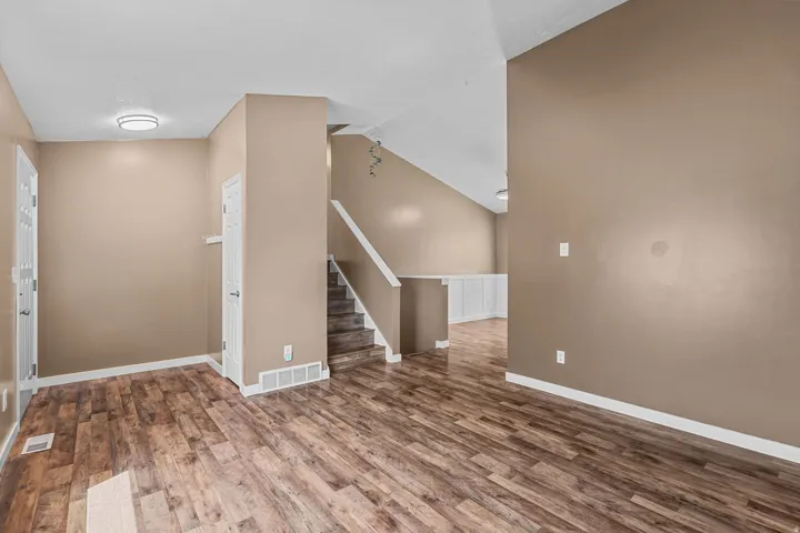 Wood-finish flooring, staircase with wood treads, vaulted ceiling, built-in white cabinetry, and flush mount lighting