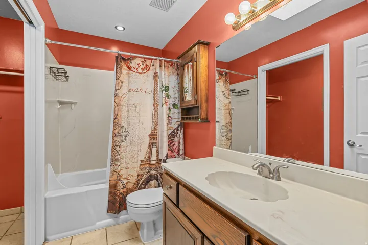 White bathtub and shower combination, vanity with an integrated sink, wood-finish cabinetry, and a full-width mirror