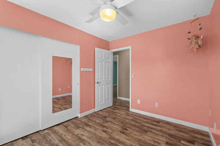 Wood-finish flooring, ceiling fan with integrated lighting, paneled interior door, and a built-in closet with an integrated mirror