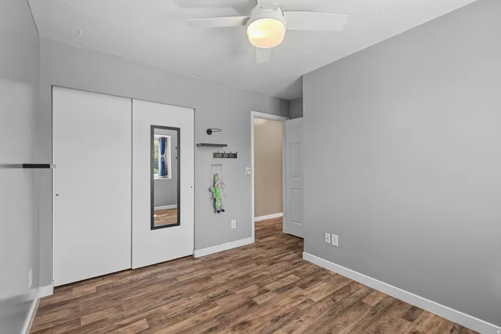 Wood-finish flooring, ceiling fan with integrated lighting, and white bi-fold closet doors with an integrated mirror