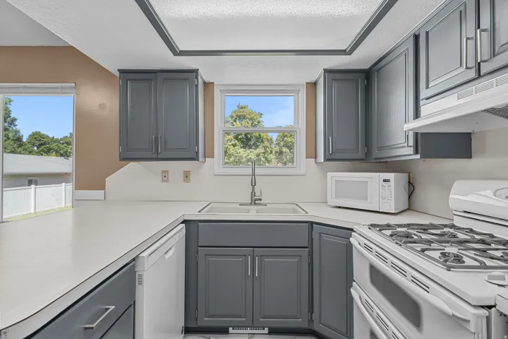 Kitchen featuring gray cabinetry, white countertops, built-in dishwasher, gas range, and a window above the sink