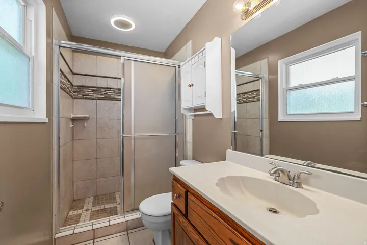 Shower with sliding glass doors, mosaic tile accent band, and tiled flooring